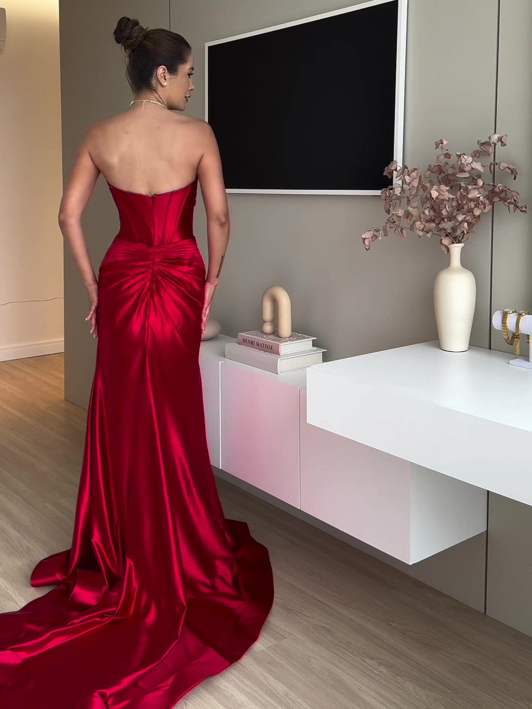 Robe de soirée longue rouge sans manches vue arrière avec traîne sur un sol en bois.