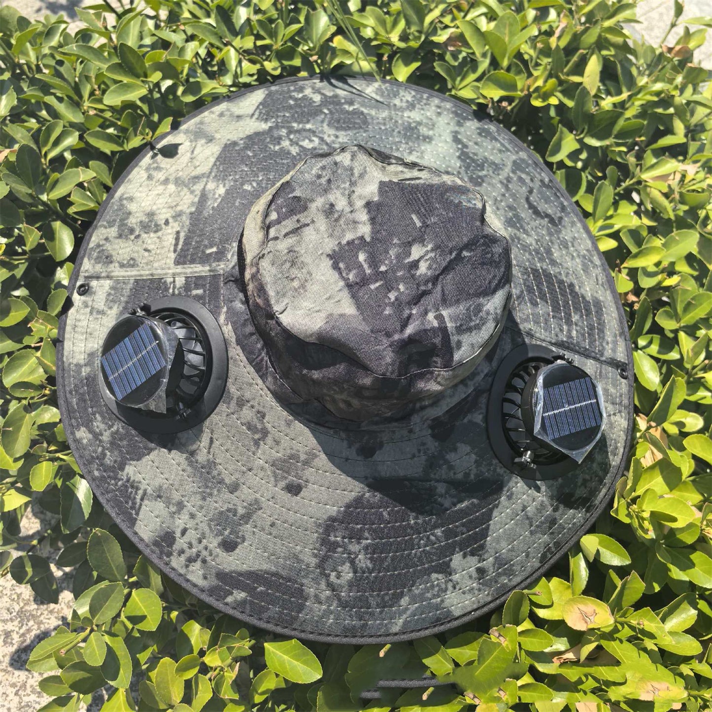 Chapeau à double ventilateur solaire posé sur des plantes, avec panneaux solaires intégrés sur les côtés.